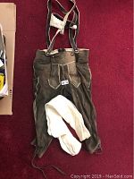 Full view of brown leather lederhosen laid flat with attached suspenders and white knit socks placed on top.
