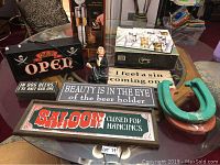Various vintage-style bar signs arranged on a glass table with a small figurine and additional decor items.