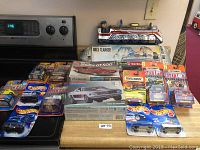 Overview of the entire toy lot showing model car kits, Hot Wheels, Matchbox cars, and the Bell Clanger tin toy on a kitchen counter.