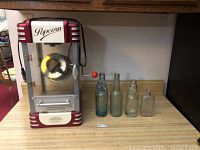 Full view of popcorn maker and four antique bottles on countertop.