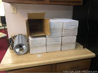 Six white cardboard boxes with one open showing a stage light; stage light cylindrical, gray with smooth ribbed metal housing and black cord.