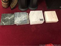 Multiple stacks of marble tiles in different colors placed on red carpeted floor: dark green, grayish, white, and beige.