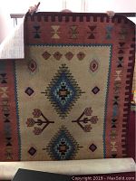Full view of the rug held up showing its rectangular shape and full design with central and border patterns.
