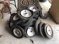 Pile of multiple wheelbarrow tires arranged on concrete floor showing variety of tire sizes and white metal rims.