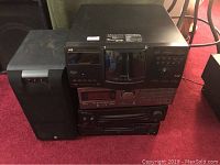 Front view of stacked stereo system components including JVC cassette deck, Kenwood CD player, amplifier, tuner, and two speakers positioned on carpeted floor.