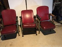 Three original Lord Baltimore Theater seats showing red vinyl cushions and cast iron frames with green paint and rust.
