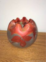 Front view of round art glass vase with ruffled rim and floral hand painting in red and orange tones on smoky glass background.