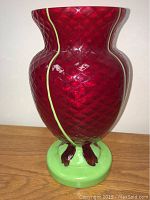 Front view of the red art glass vase showing diamond pattern, yellow accent line, green base and red feet.
