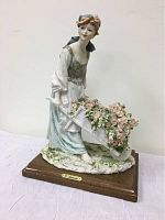 Porcelain figurine on wooden base showing full figure of woman pushing wheelbarrow with roses.