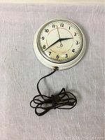 Front angle view of the Westclox electric clock on a white fabric background, showing face and attached brown power cord.