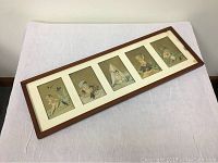 Full view of the framed lot showing all five baby-themed Victorian cards inside a wooden frame on white mat.