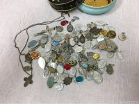 Spread of over 100 vintage Catholic religious medals and small pendants on a light background, showing variety of shapes and colors including silver-tone, gold-tone, and colored enamel.