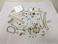 Full assortment of jewelry spread on white cloth, shows variety of necklaces, bracelets, earrings, rings, charms and brooches