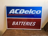 Full view of vintage metal painted AC Delco Batteries sign showing blue and red sections with white lettering.