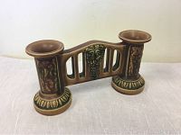 Side angle view of double candle holder showing the cylindrical candle holders and middle decorative panel with grapevine motif.