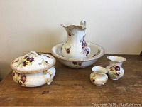 Full set showing pitcher with repairs, bowl, chamber pot with lid, small shaving cup, and small vase all on wooden surface