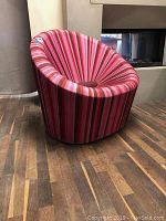 Side, angled view of circular chair showing pink, red and cream vertical stripes fabric and rounded form.