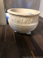 Side view of cream colored concrete planter showing textured surface and decorative scroll design around the upper band.