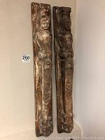 Full view of the two vertical concrete wall decor panels leaning against wall, showing full length and aged finish.