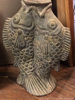 Full front view of concrete vase with double fish design on a wooden floor.