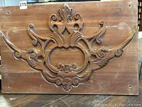 Front view of one antique wooden panel with hand carved raised floral and scroll designs, showing missing carved arms and dust on surface.