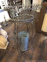 Front perspective of the antique wire fern stand showing twisted and straight wire design with metal flower bucket placed inside on lower shelf.