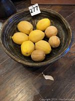 Top-down view of dark ceramic bowl containing artificial fruit including lemons and nuts
