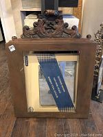 Front view of the brown painted rectangular wooden frame with carved decorative top and new unattached mirror inside.