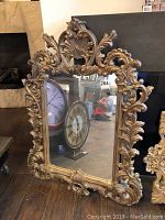 Front view of large mirror with ornate gold-toned molded frame showing detailed carvings and reflective glass.