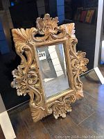 View of the entire small carved mirror showing the molded and antiqued frame with intricate floral and scroll motifs around the rectangular mirror glass.