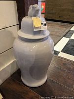 Front view of large white ceramic covered jar with dog-shaped handle on lid showing glossy ceramic surface and tag.