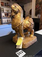 Side angle view showing horse's left profile, gold finish with some chipping revealing rust paint underneath; placed on rectangular base.