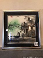 Framed original watercolor painting showing a riverside scene with buildings, boat, and tree with green background wash.