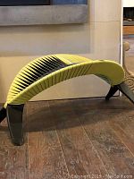 Photo of the sculpture chair showing the side view with leaf-shaped yellow and black slatted seat and black legs on wooden floor.