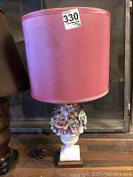 Front view of the full lamp showing pink silk shade and white ceramic floral base with some damage.