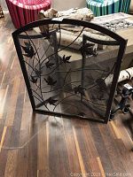 Front view of the black metal fire screen with leaf design and mesh insert, showcasing the metal branches and leaves pattern.