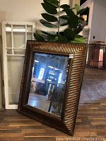 Full view of the large beveled mirror leaning against a wall near furniture and greenery.