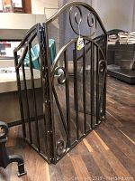 Full view of folded three-panel steel fireplace screen with brown-toned metal and decorative scrollwork.