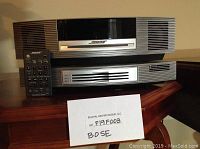 Two stacked titanium silver Bose Wave units (main system and multi-CD player) with remote control and lot sign