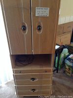 Front view of oak armoire cabinet showing closed double doors with oval handles over two drawers and a pull-out table below the storage compartment.