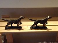 Two bronze/brass setter pointer dog door stops on a table, showing their profile and size.