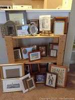 Wooden shelving unit holding various picture frames and framed prints in different sizes and styles.