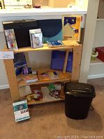 Full view of shelving unit with items including paper shredder, file organizers, office supplies, note cards, Logitech headset in box, and picture download device.