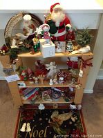 Wide view of assorted Christmas decorations displayed on wooden shelving including Santa Claus doll, nativity set, angels, and other holiday figurines.