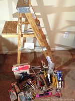 Photo of the 4-foot wooden step ladder with assorted hand tools and hardware placed around it on carpeted floor.