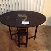 Front view of dark wooden antique drop leaf table with visible water stain on top and four legs with stretchers