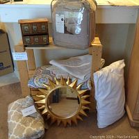 Photo showing entire lot including folded sofa cover, plush sheet set in packaging, two folded matelasse coverlets, gold sunburst mirror in front, white pillow, and wooden jewelry box on shelf top