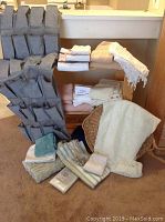 Full view of gray over-the-door organizer with many pockets, towels in neutral colors stacked, lace curtain panels on chair back, rattan tray visible partially