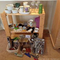 Overall photo showing wooden shelf with assorted kitchen items including ramekins, mugs, glasses, utensils, graters, and knives.