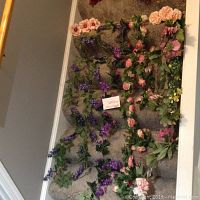 Photo showing multiple silk floral swags including purple and pink roses laid out on carpeted stairs